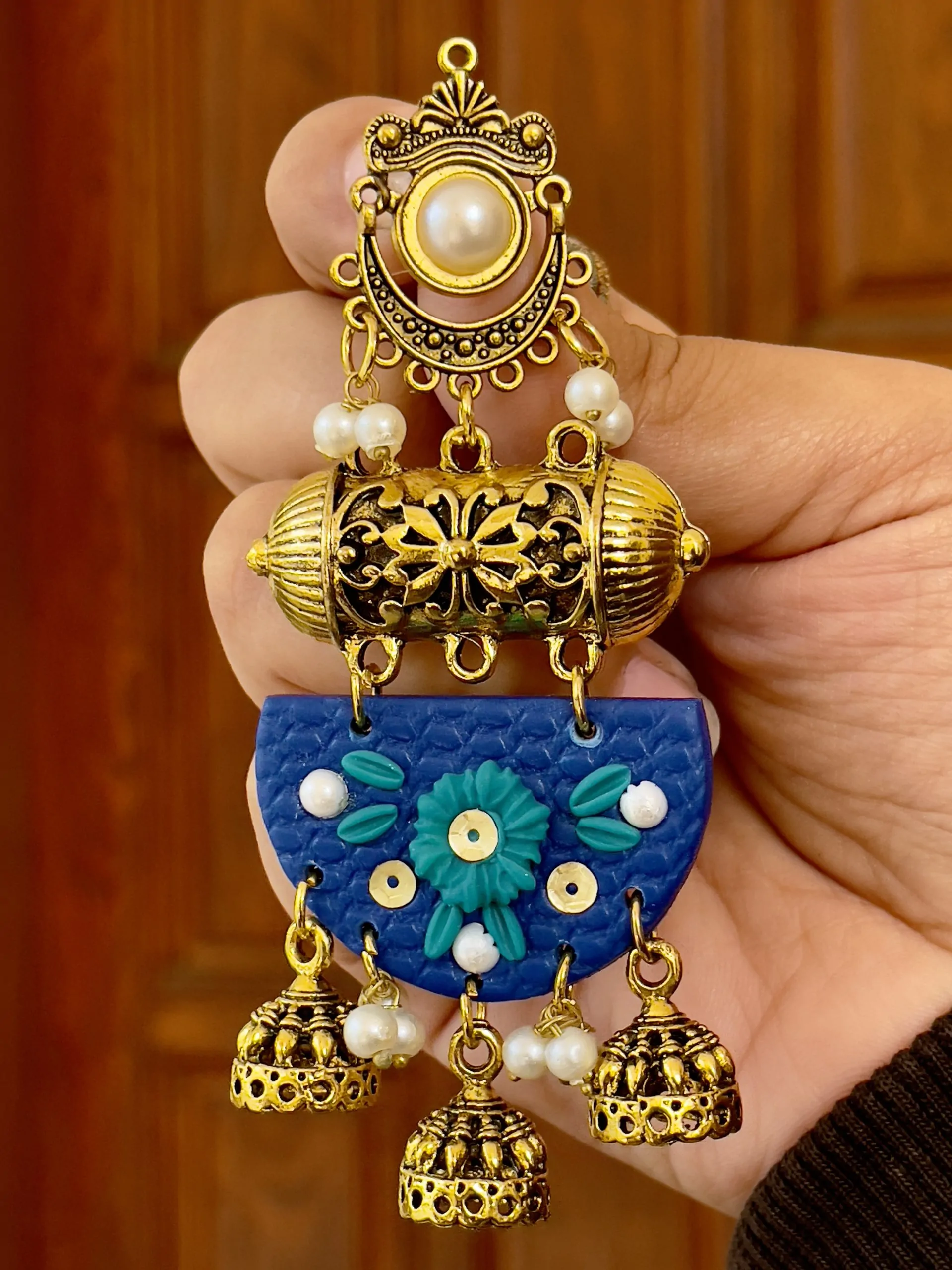 Close-up of textured blue half-moon earrings with teal flowers and gold-toned traditional dangles.