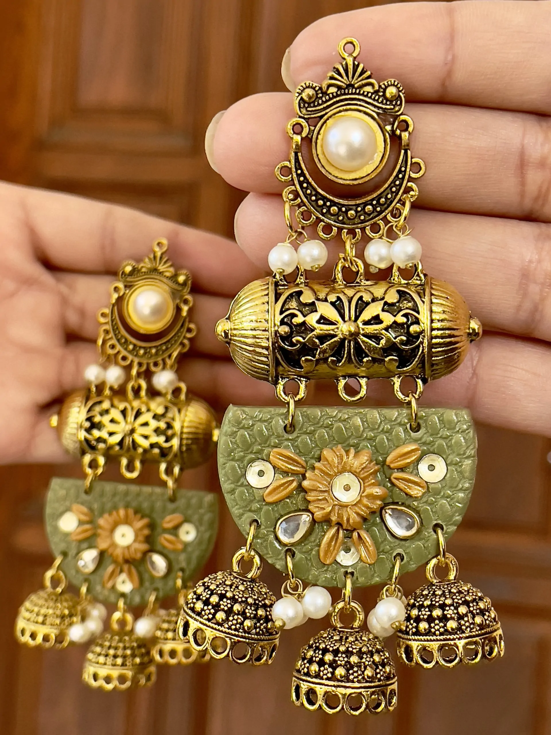 Olive green textured half-moon jhumkas with mustard flowers and five gold bell drops.